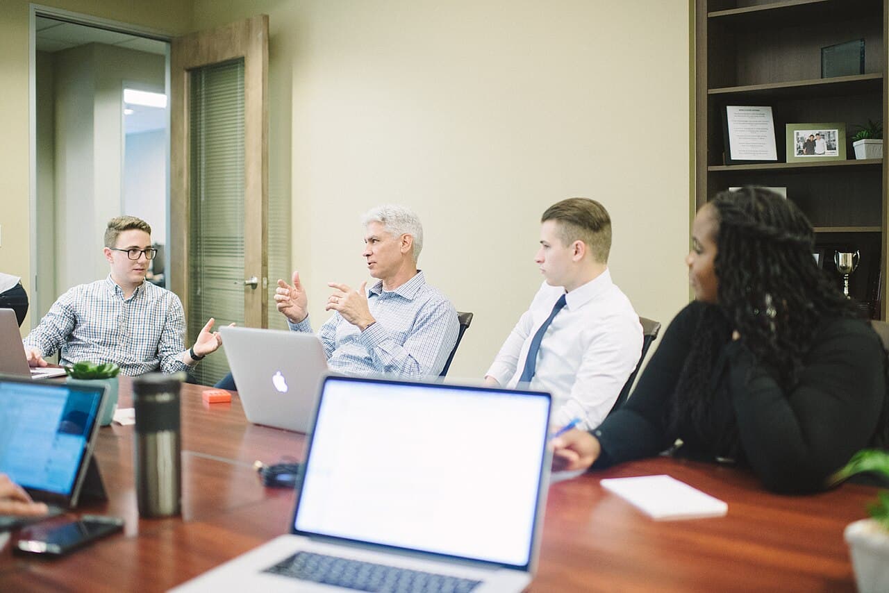 A team meeting around a table, the kind of conversation where work actually gets reassigned